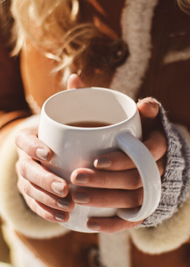 A person in a cozy jacket holds a white mug with both hands, likely containing a warm beverage, creating a comforting scene.