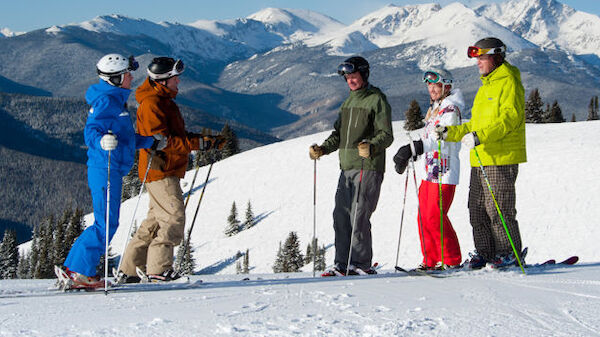 A group of skiers stand together on a snowy slope with mountainous terrain in the background, ready to hit the slopes.