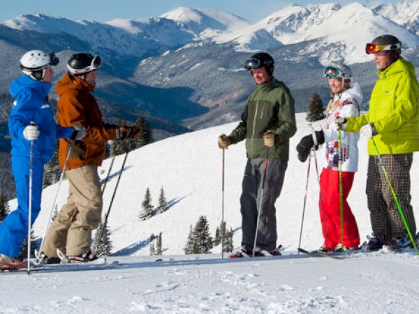 A group of skiers stand together on a snowy slope with mountainous terrain in the background, ready to hit the slopes.