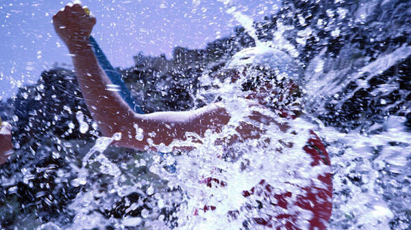 A person is captured mid-action as they are splashed with water, raising their arm in what appears to be an energetic or playful moment in nature.