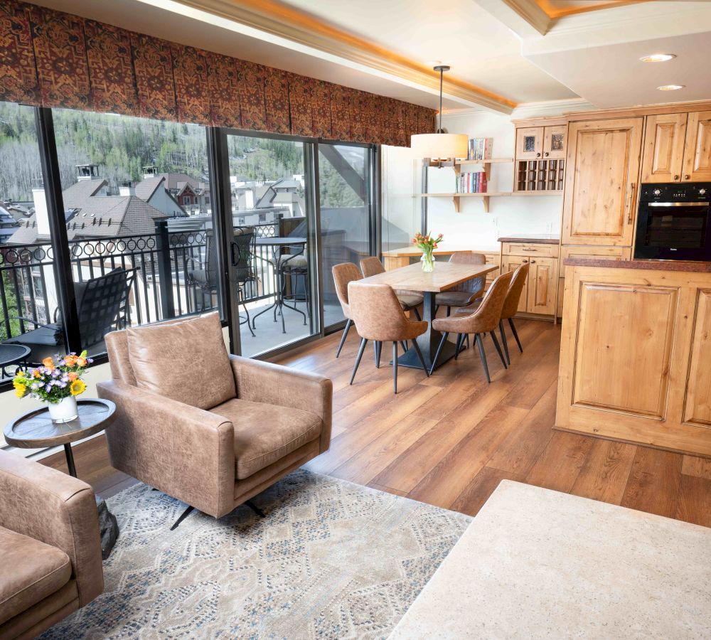 A cozy living room and kitchen combo featuring wooden cabinetry, a dining table, comfortable seating, and large windows with a scenic view.