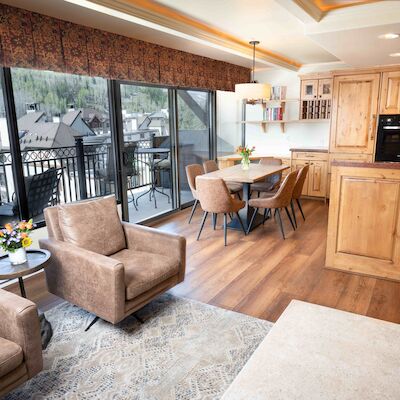 A cozy living room and kitchen combo featuring wooden cabinetry, a dining table, comfortable seating, and large windows with a scenic view.