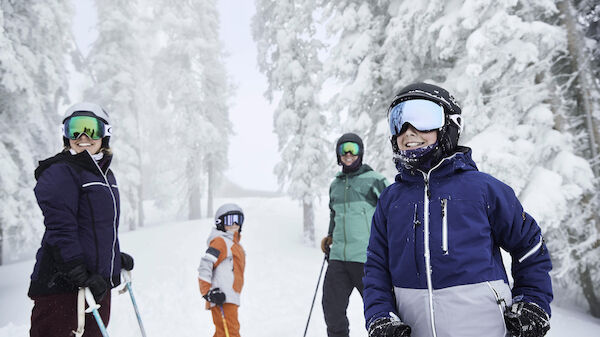 A group of people in ski gear smiles in a snowy, forested landscape. They appear to be enjoying a winter day in the mountains, posing for a photo.