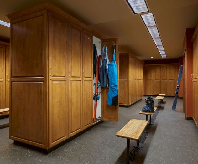 The image shows a locker room with wooden lockers, benches, some hanging clothes, and a pair of boots on the floor.